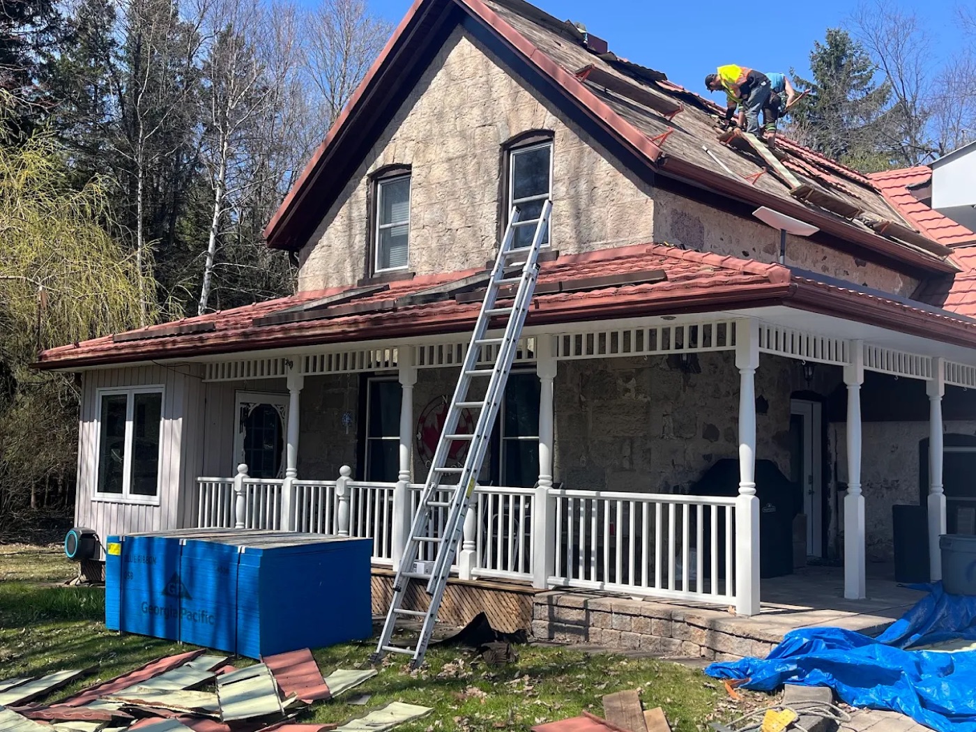 Roofer installing a red metal tile roof on a stone farmhouse, secured on a safety line