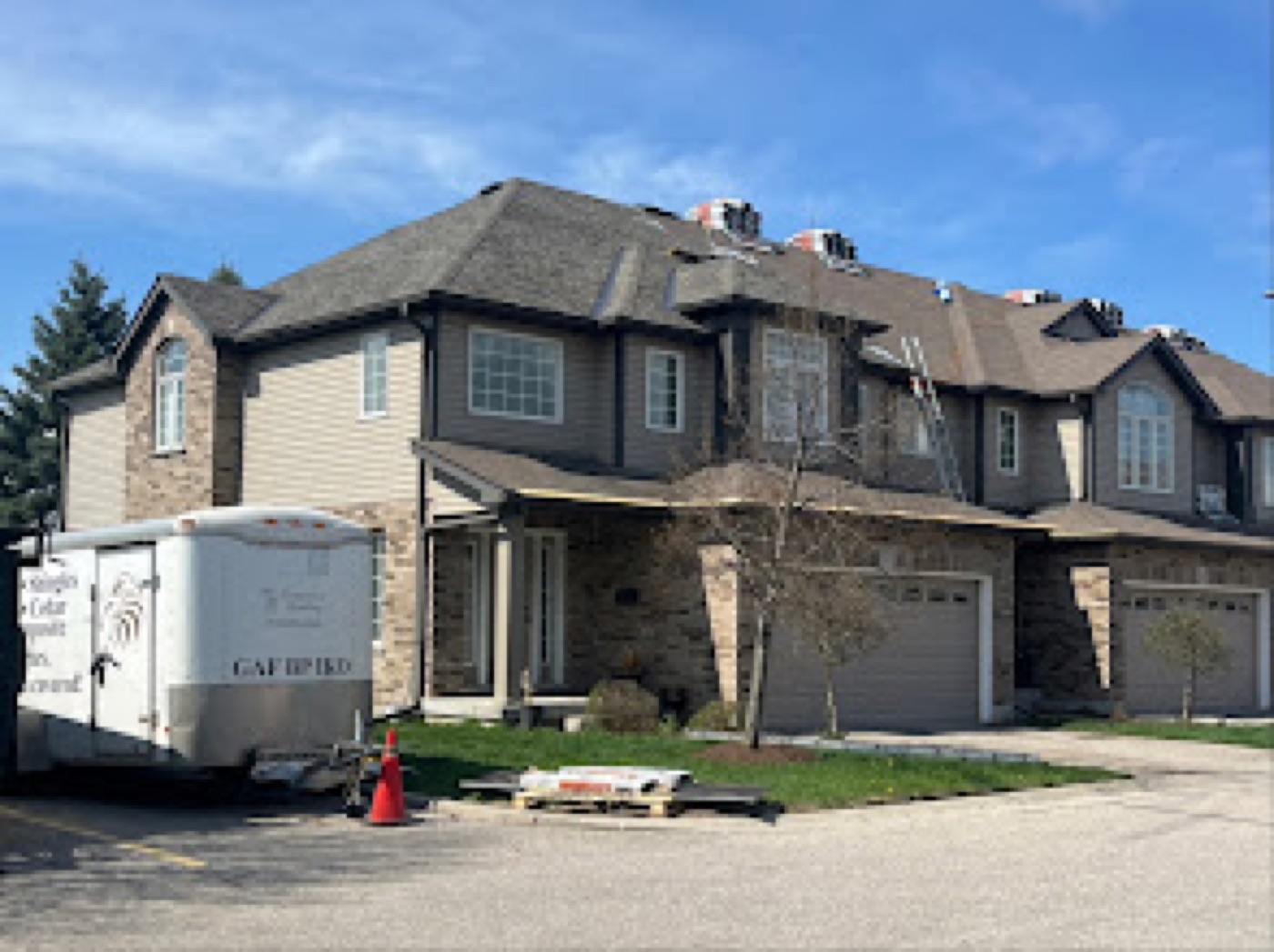 Testarossa Roofing crew re-roofing a townhouse with a GAF-certified trailer parked in the driveway